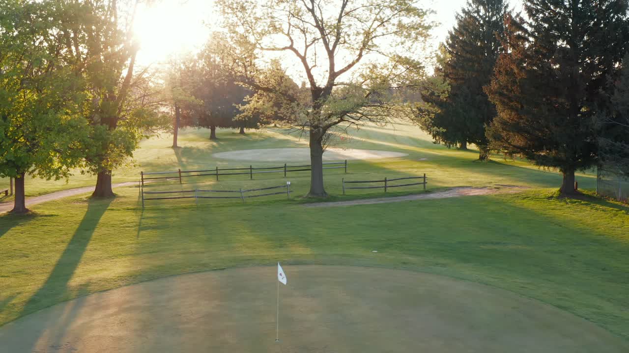 Golf course putting green, white pin flag waves in breeze during sunrise