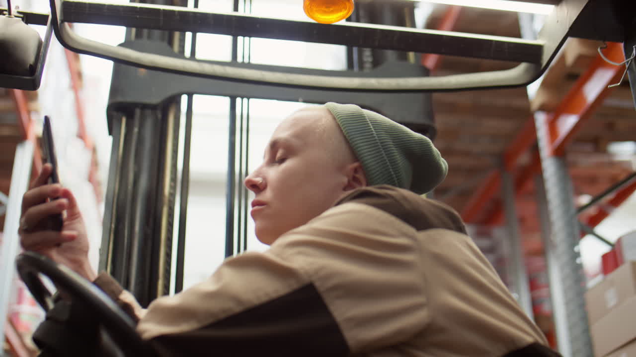 Person operating a forklift and using a smartphone in a warehouse