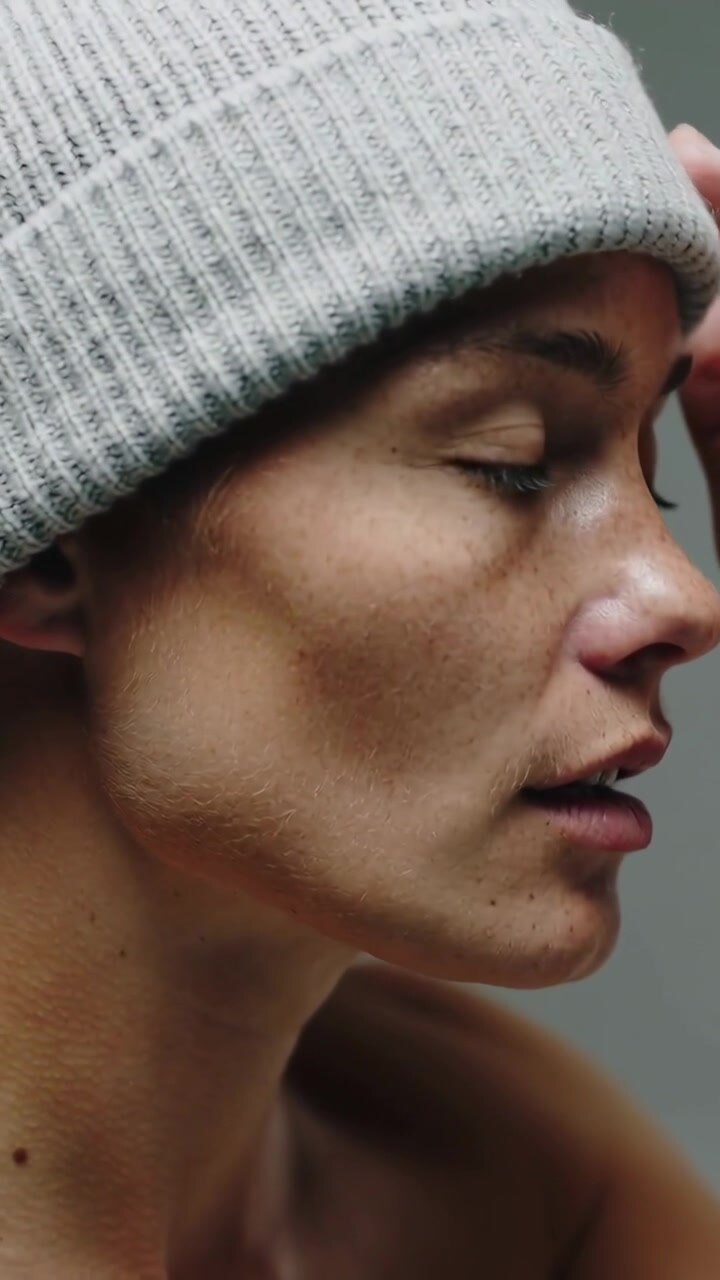 Vertical video: Tilting adult male shifting jaw then raising right hand in studio, adjusting beanie