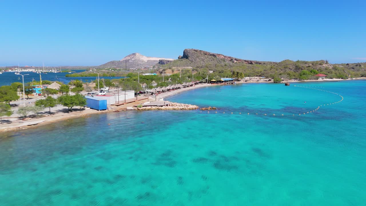 Aerial establishing of Caracasbaai Beach, Curacao, sandy shorelines meet vibrant turquoise waters under clear skies