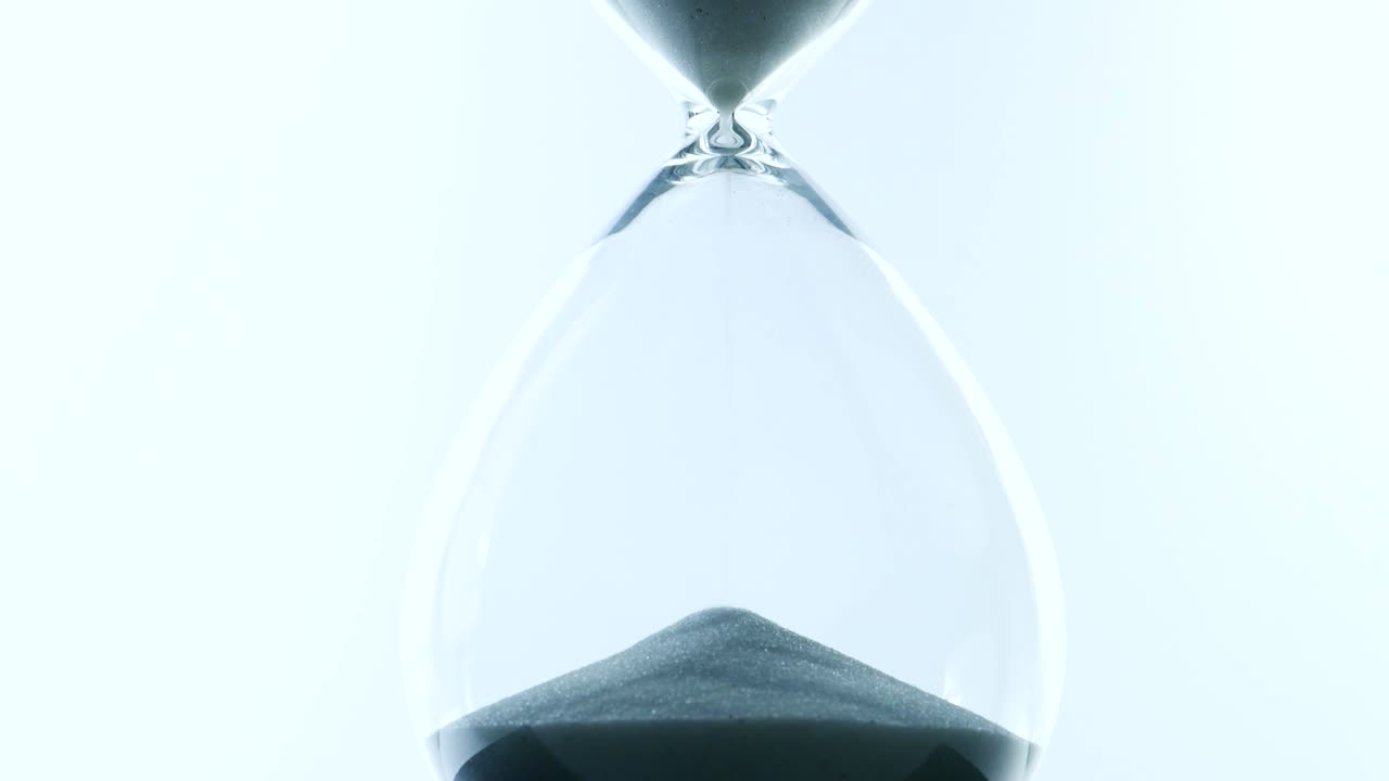 Close up, Sand pouring into the glass jar called hourglass.