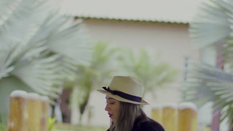 lady in a straw hat puts a glass and bottle of red wine on a table in the garden with palm trees - close up slow motion