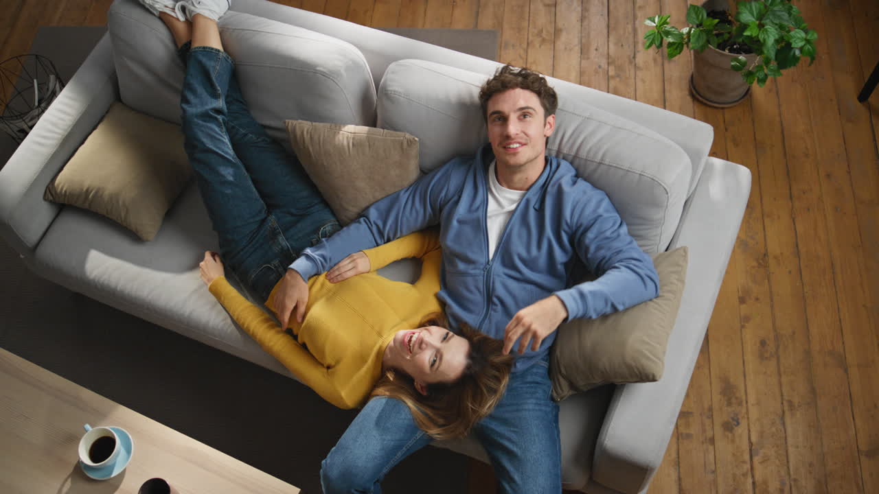 Cheerful couple dreaming together at sofa top view. Man pointing finger talking