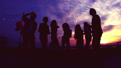 silueta de personas celebrando con amigos festejando juntos en la azotea. hombre y mujer disfrutan bailando y bebiendo en fiesta con un cielo dramático. concepto de festival, feliz año nuevo y navidad. resolución 4k.