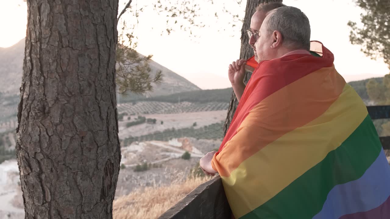 Man with gay pride flag overlooking mountain landscape