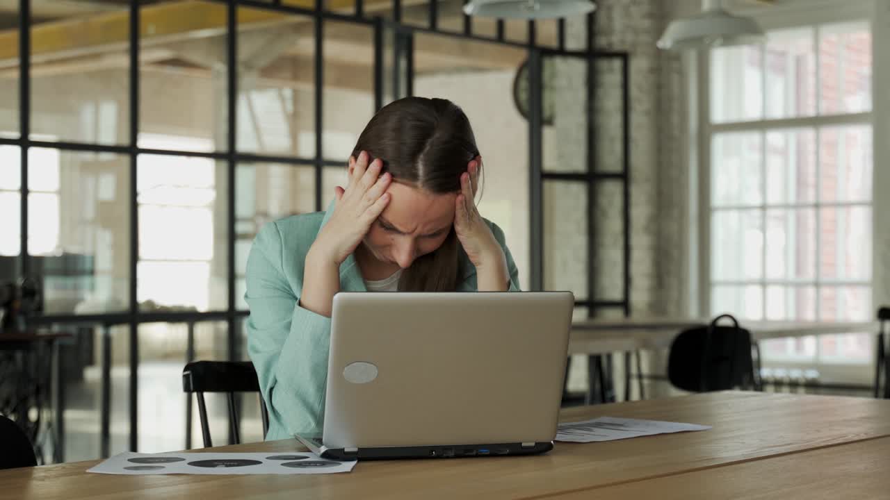 노트북을 가지고 사무실에 앉아 프로젝트를 하는 동안 문제를 겪고 있는 분노한 여성이 종이 문서를 던집니다.