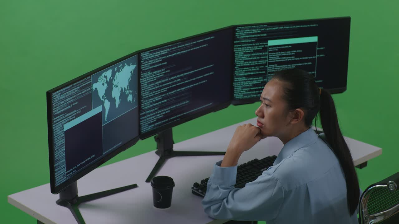 Side View Of Asian Woman Developer Thinking About Something Then Raising Her Index Finger While Write Code With Multiple Computer Screens In Green Screen Studio