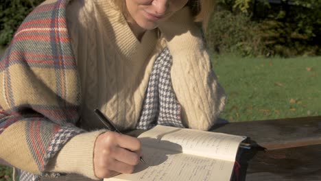 woman wearing sweater writing at park bench