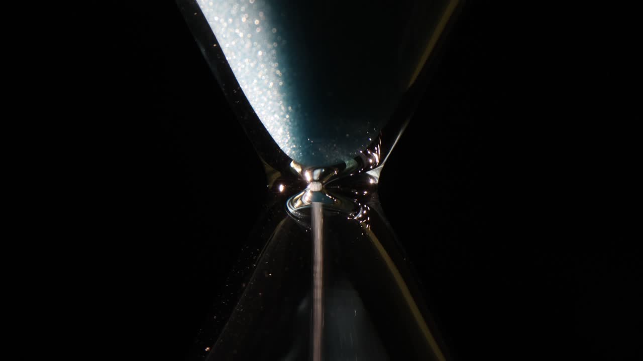 Close-up of Sand Flowing in an Hourglass on a Dark Background