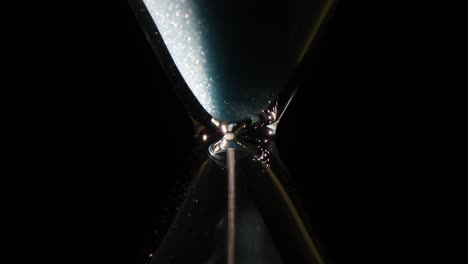 close-up of sand flowing in an hourglass on a dark background