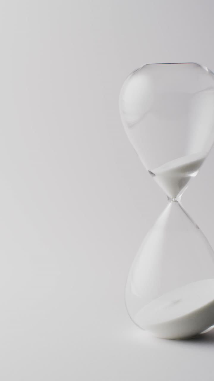 Vertical video of hourglass with sand pouring, copy space on white background