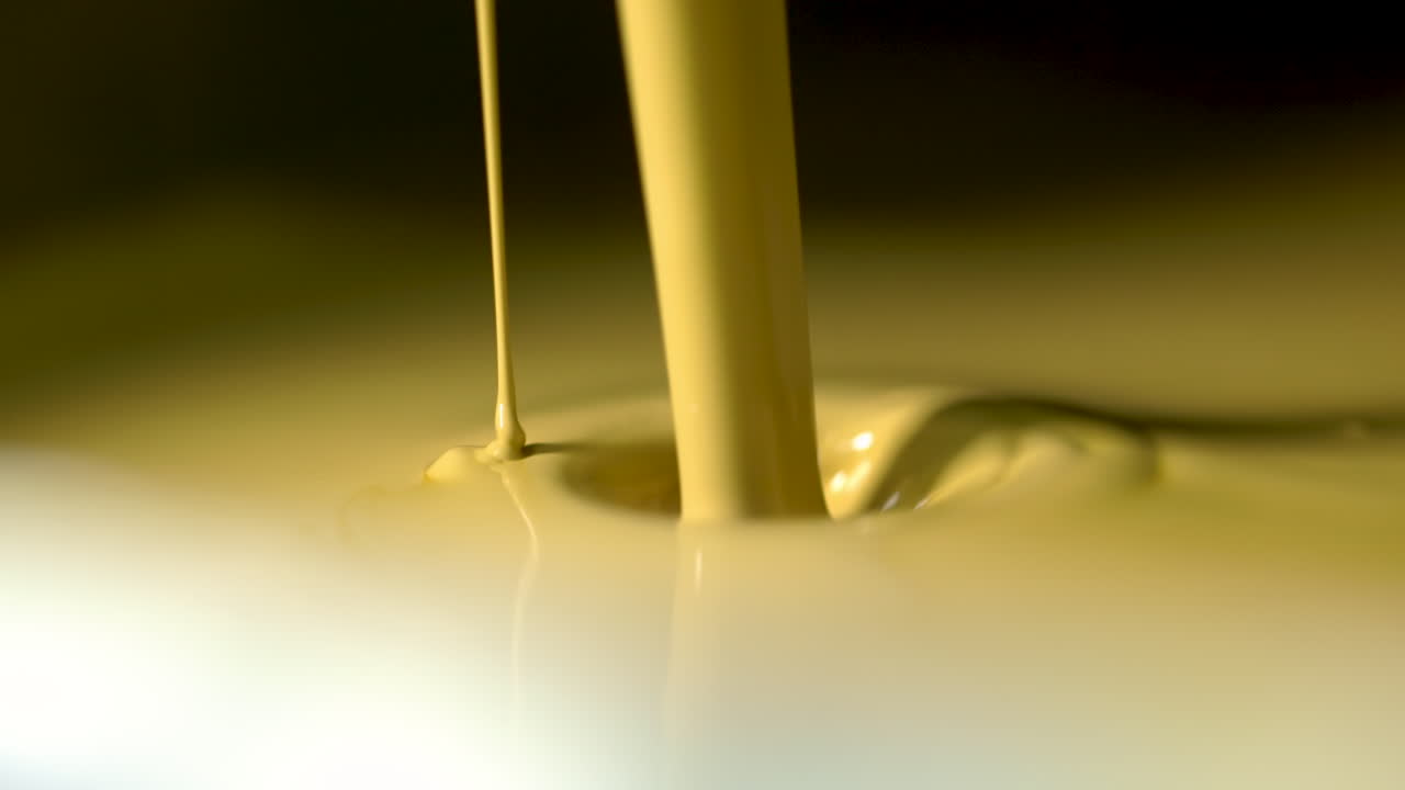 Extreme closeup of pale yellow paint endlessly pouring into a enclosure of paint