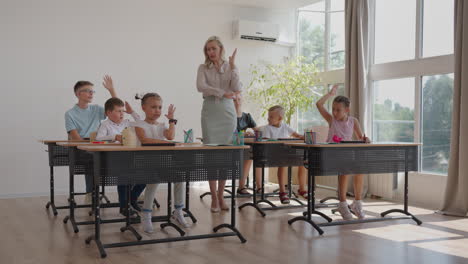 the teacher walks around the classroom of the school. a group of children is sitting at their desks. children write down the task. an elementary school lesson in slow motion. perform control work