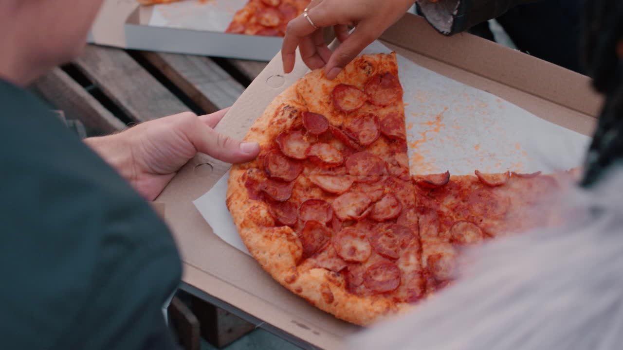 옥상에서 피자를 먹고 주말 파티를 즐기는 친구들 그룹이 함께 대화를 나누고 일몰 때 축하를 나누고 있습니다.