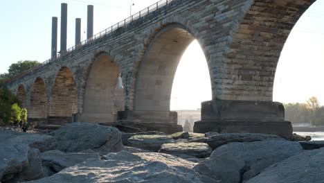 People-Exploring-Riverbed-During-Drawdown-Under-Stone-Arch-Bridge