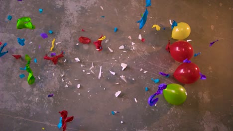 a plate being dropped in the middle of colorful balloons and it breaks in pieces and the bits and shards shatter and make balloons explode around it in slow motion. view from the top, concrete floor.