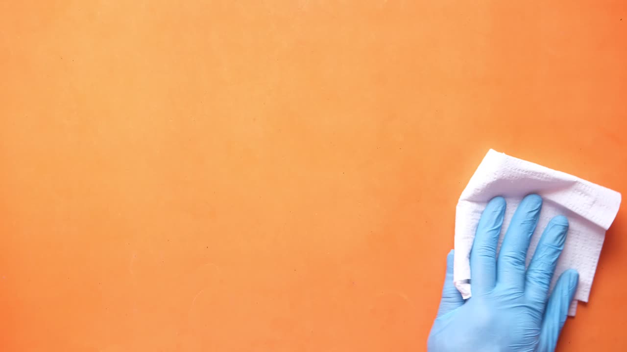 limpiando una superficie naranja con guantes azules y un paño blanco
