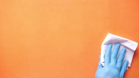 limpiando una superficie naranja con guantes azules y un paño blanco