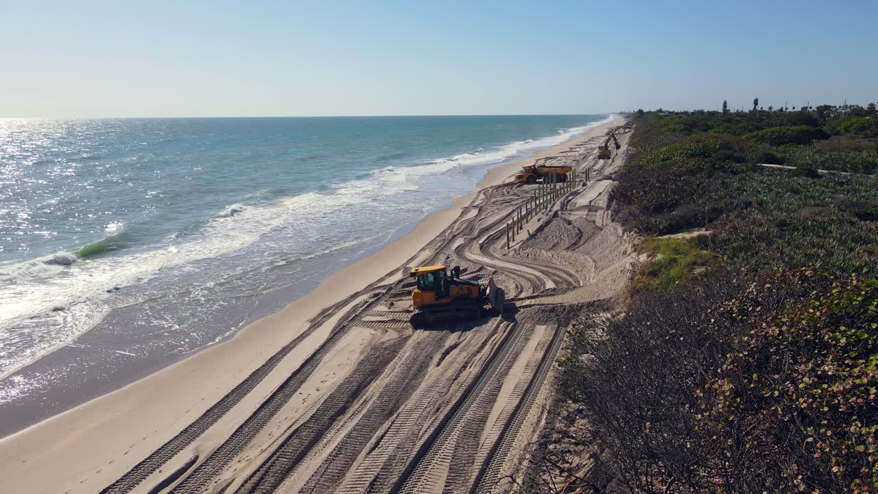 disparo de drones de excavadoras y camiones volcadores trabajando en la playa cerca de la orilla con olas azules que se estrellan cerca de la orilla