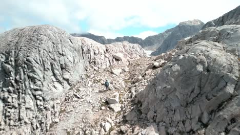 Persona-Caminando-Mientras-El-Dron-Pasa-Y-Luego-Gira-A-La-Derecha,-Lo-Que-Le-Permite-Ver-Un-Gran-Valle-Remoto-Que-Comienza-En-Una-Laguna-Azul