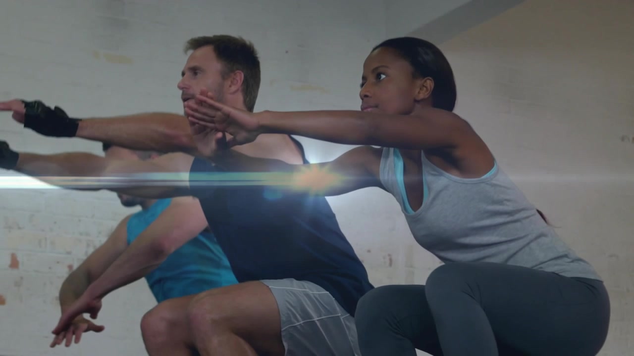 Center male starting arm swing, trio performing jump squats in fitness for training, showing gloves