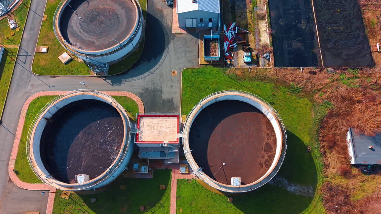 Symmetrical top view of secondary clarification tanks. Close up aerial perspective of circular water treatment tanks with dark liquid and technical walkways