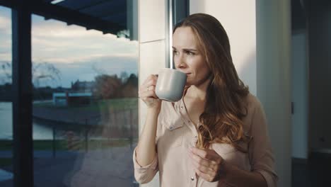 Relaxed-woman-staying-near-window-after-working-day.-Pretty-lady-watching-sunset