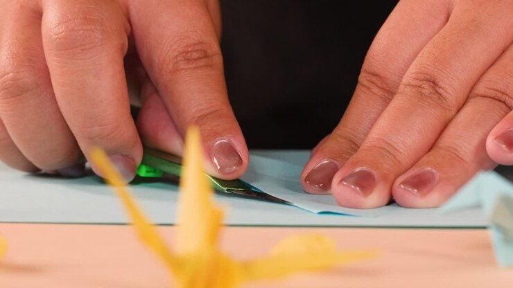 Close-up shot of hands carefully folding and creasing blue paper for an origami project