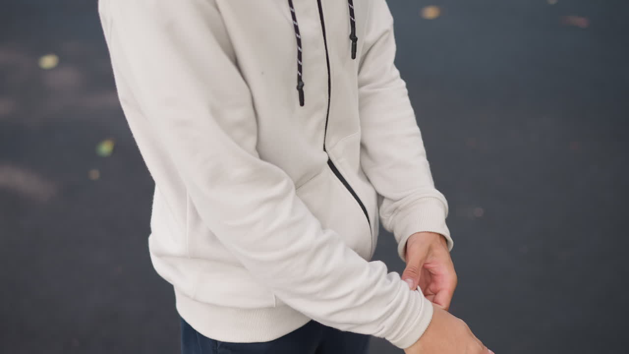 hombre caucásico remangándose antes de la lluvia, preparándose para la llovizna en la acera mojada, movimiento rápido de la muñeca, cremallera y bolsillos visibles, reflejos en los charcos, cielo nublado, energía enérgica y confiada, moderno