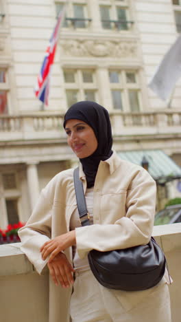 vertical video portrait of smiling muslim businesswoman wearing hijab and modern business suit standing outside city office buildings 7