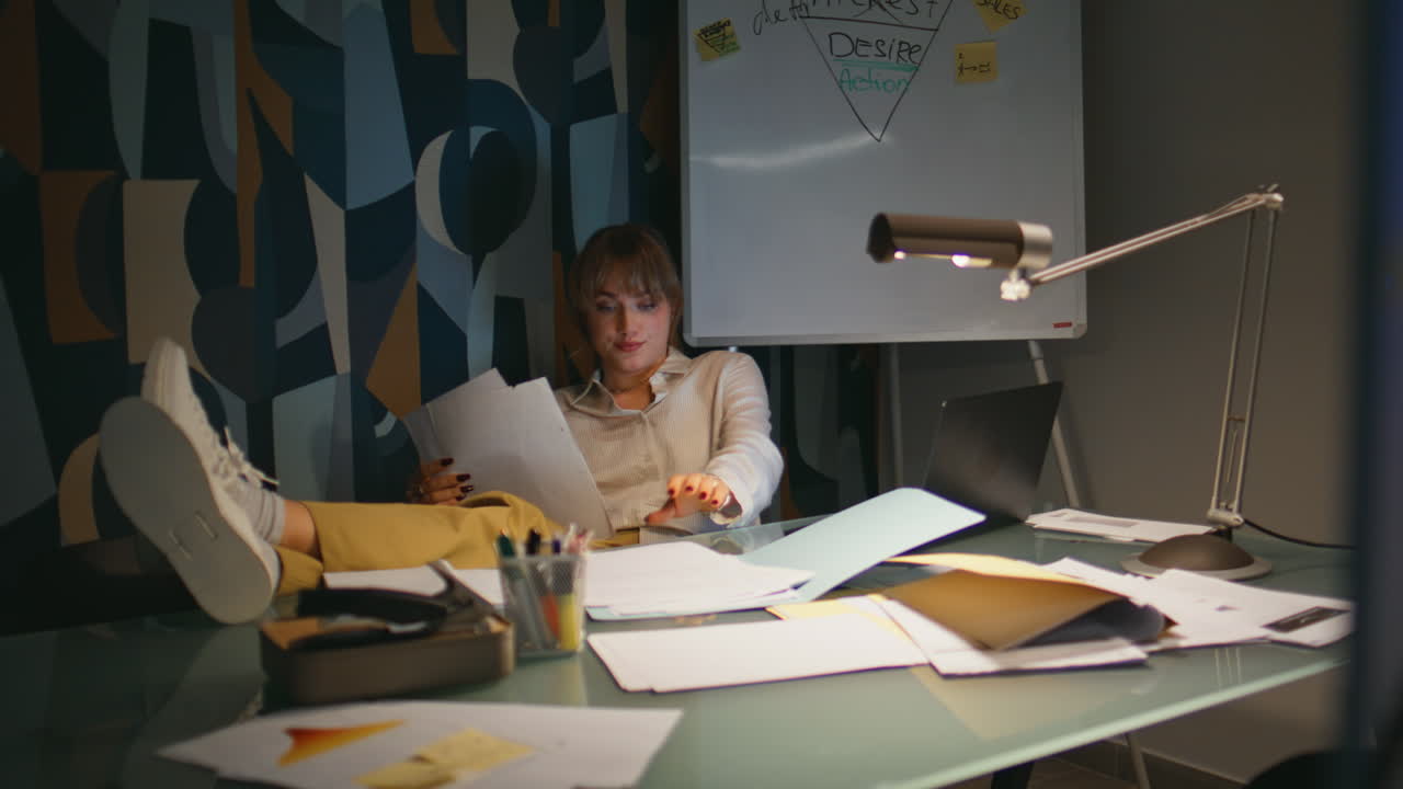 Late businesswoman messaging mobile phone night office. Lady with legs on table