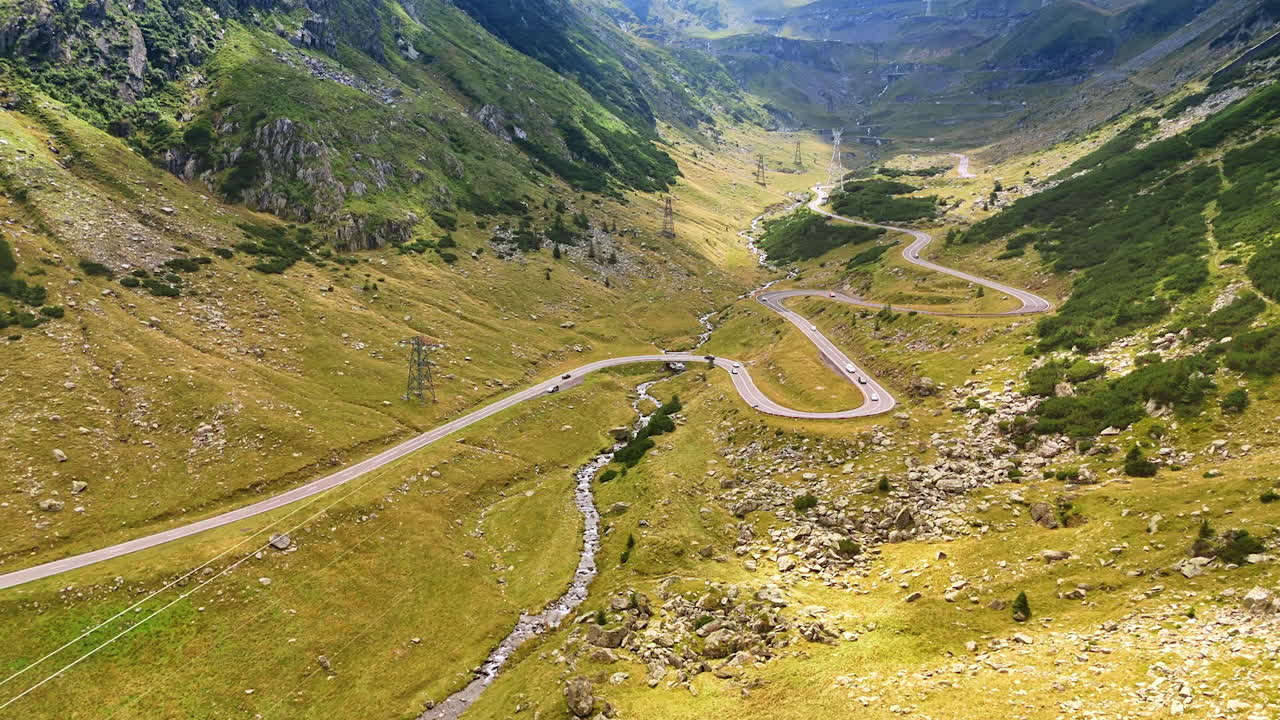 Flight over the valley crossed by the famous Transfagarash highway. Cars ride by the road at daytime. Landmark of Romania
