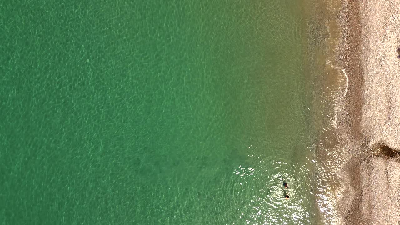 Aerial top view of beautiful coast line at Verga beach, Kalamata, two caucasian boys enjoying the crystal clear waters 4K