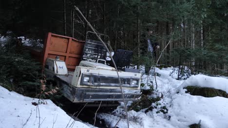 a young man walks around a forest machine which stuck inside the snow, he wears a black coat