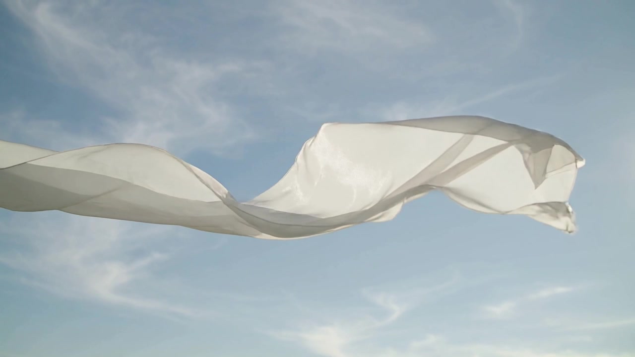 Tessuto bianco che fluttua, si allunga, si avvolge e si gonfia sopra il cielo blu mentre la brezza lo solleva, illuminato dal sole.
