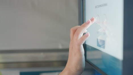 close up female hands reach to payment kiosk screen inside laundromat, tapping icons, blue glow on fingers, contactless self service interface, cashless transaction, technology