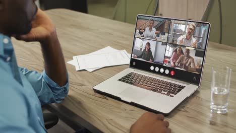 African-american-man-using-laptop-for-video-call,-with-diverse-business-colleagues-on-screen