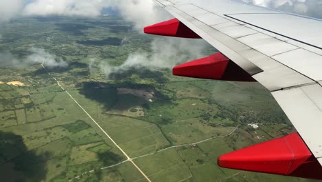 view through passenger window on airplane wing, green, flat landscape emerging from clouds