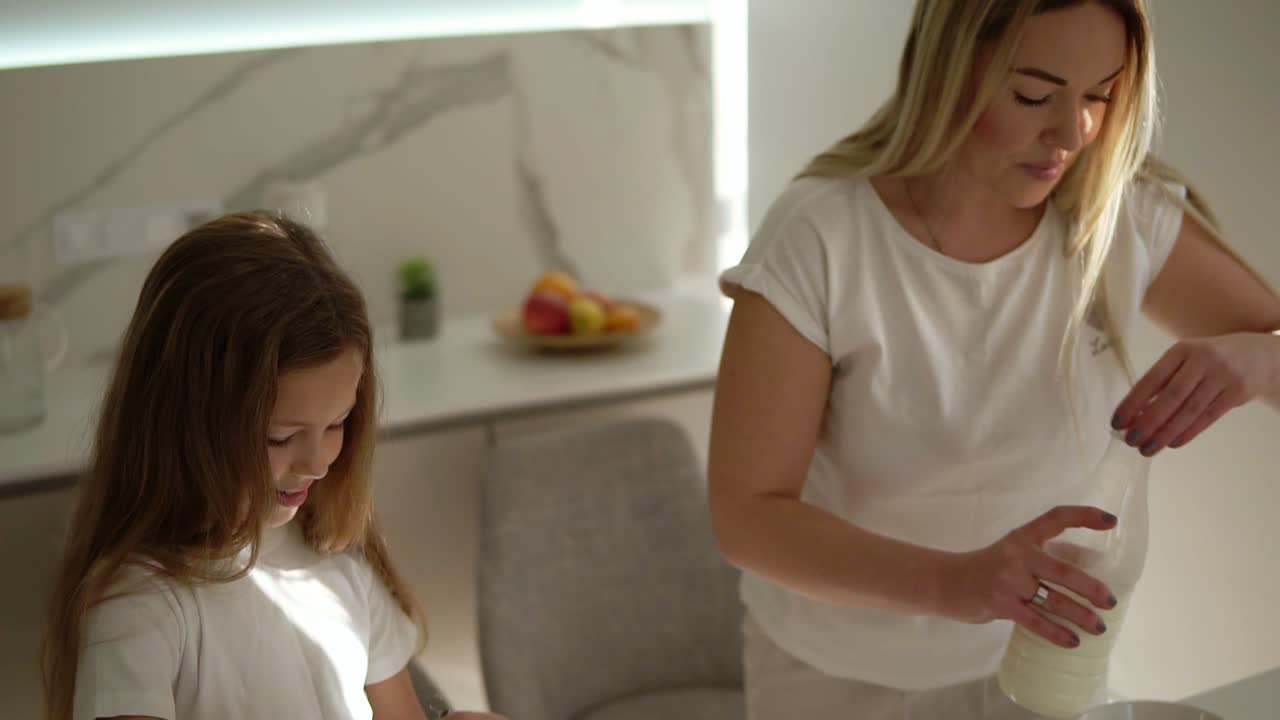 어머니는 현대적인 아 ⁇ 한  ⁇ 색 부 ⁇ 에서 귀여운 딸에게 케이크나 팬케이크를 요리하는 것을 돕고 가르치고 있습니다. 소녀는 우유를 첨가하고 재료를 혼합합니다. 행복한 가족. 관계 엄마와 딸