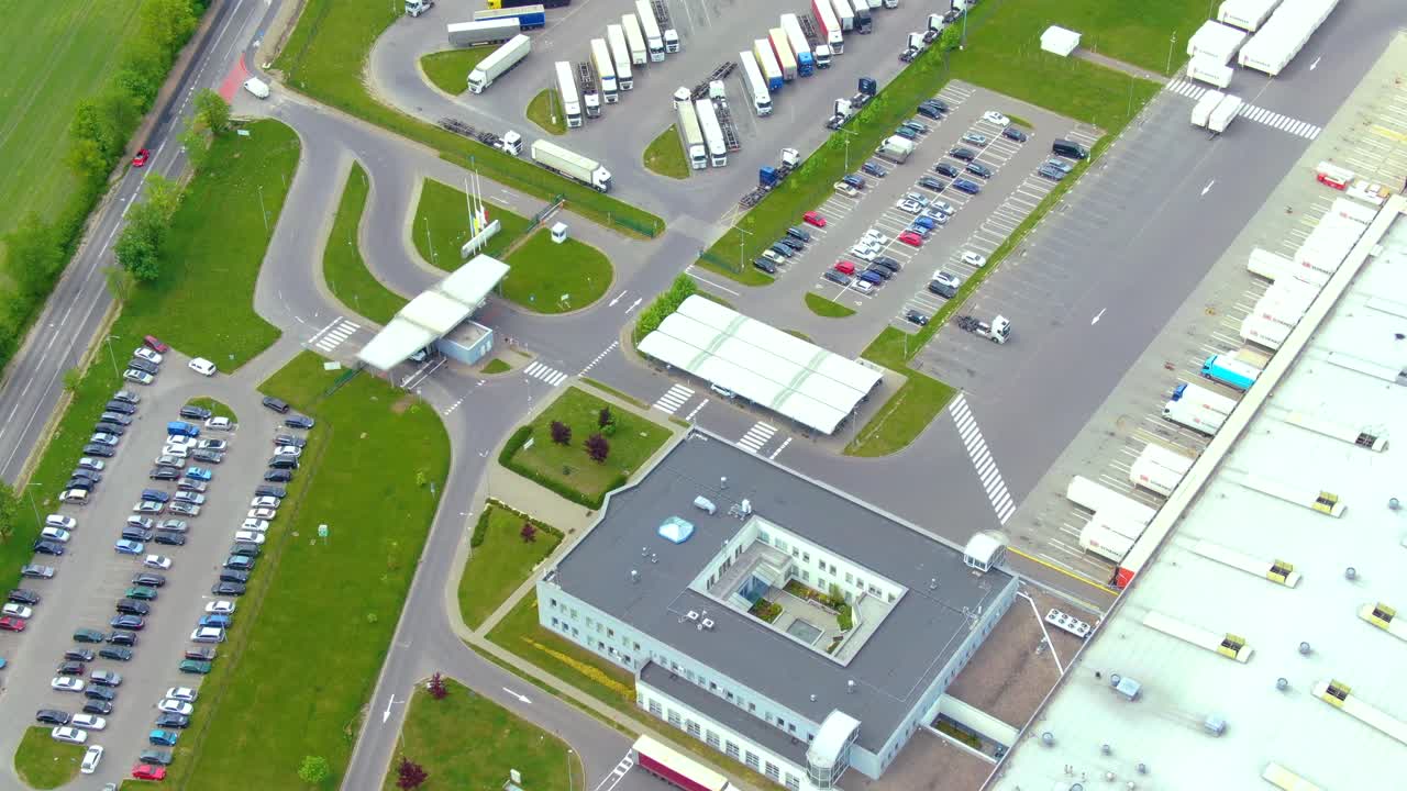 Vista aérea superior de um grande parque logístico com armazéns, centro de carregamento e muitos caminhões semirreboques com carretas de carga aguardando para carregar ou descarregar mercadorias nas rampas