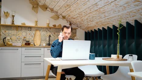 el joven está contestando el teléfono. trabajando desde casa con una computadora portátil