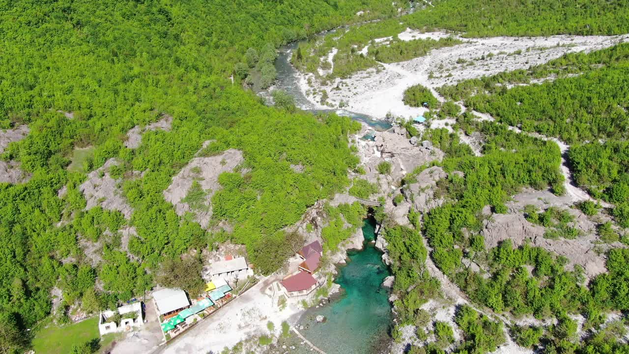 vista del avión no tripulado en albania en los alpes volando sobre el valle verde con puente colgante sobre el río de agua azul en el
