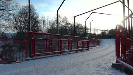 un puente con barandillas metálicas rojas durante el invierno en laagri, estonia, que está cubierto de nieve gruesa y blanca mientras el sol se pone o se levanta en el fondo.