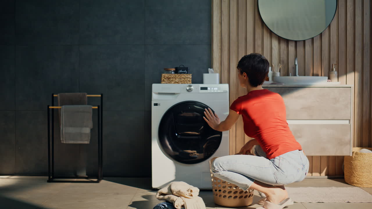 Girl turning washing machine enjoying domestic chores in sunny apartment laundry