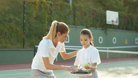 Frau-Bringt-Ihrer-Tochter-Bei,-Wie-Man-An-Einem-Sonnigen-Sommertag-Mit-Einem-Tennisschläger-Ball-Schlägt