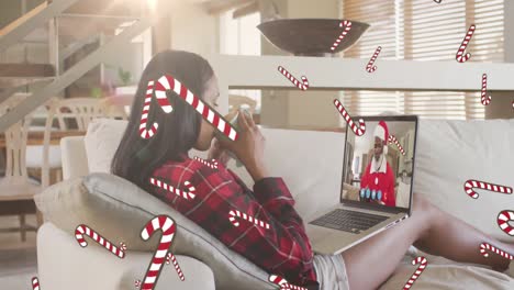 Candy-cane-icons-over-woman-drinking-coffee-and-having-a-videocall-on-laptop-during-christmas