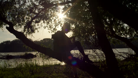 silhouette of a musician playing guitar by a river at sunset