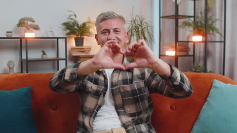 smiling man at home makes symbol of love showing heart sign to camera express romantic feelings