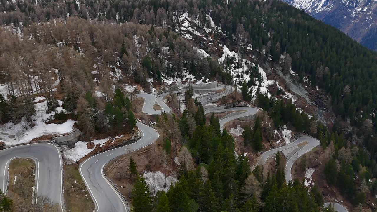 Aerial View captures a scenic winding mountain road amidst a forest landscape, with patches of snow visible, providing a stunning view of nature's beauty and complexity in winter