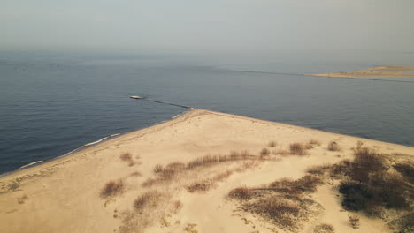 Aerial-backwards-shot-of-Baltic-Sea-with-small-jetty-and-sandy-island-during-foggy-day